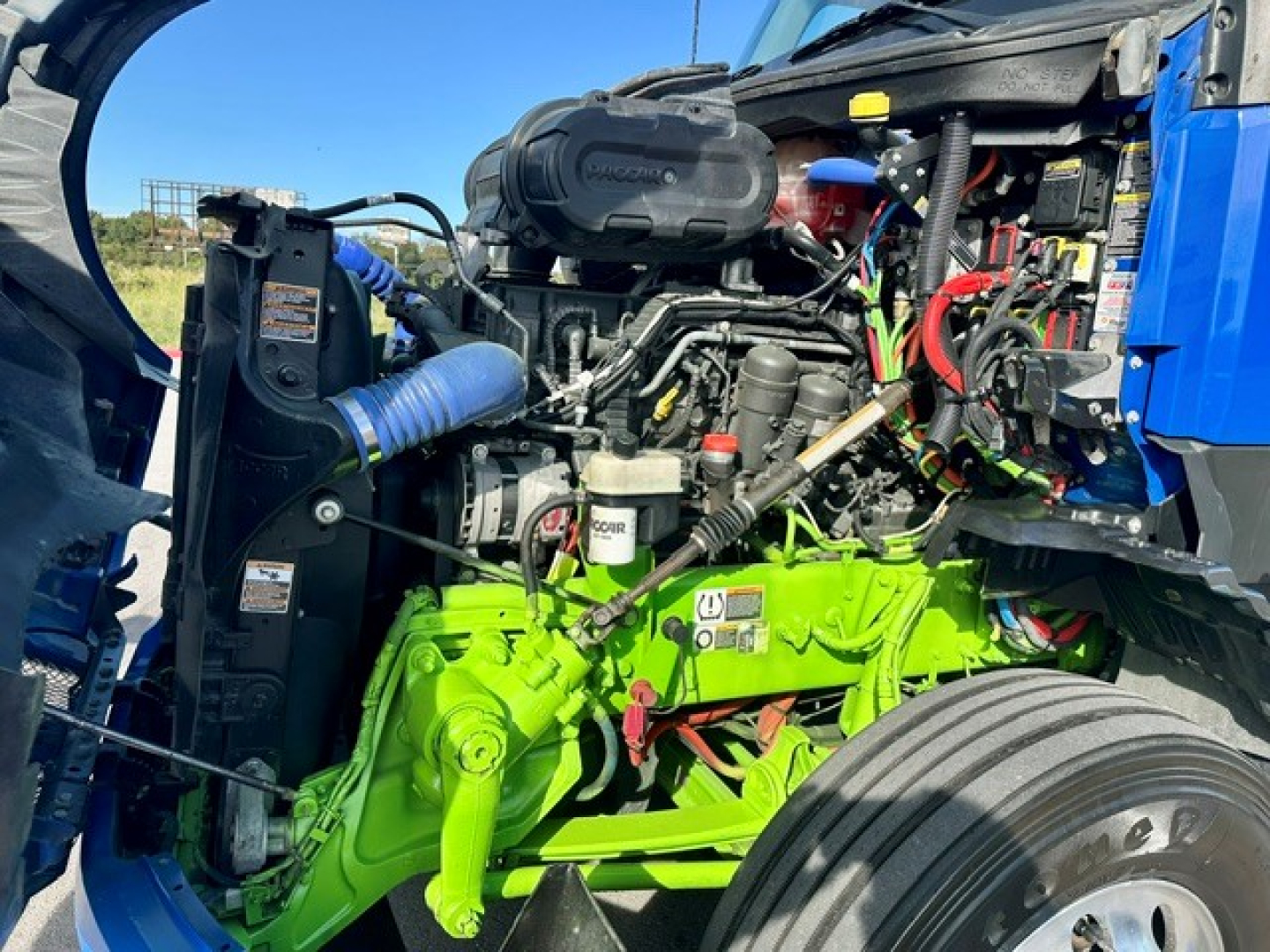 Engine bay of a Kenworth T680 with bright green engine block, hoses, and various components visible in the open hood area.