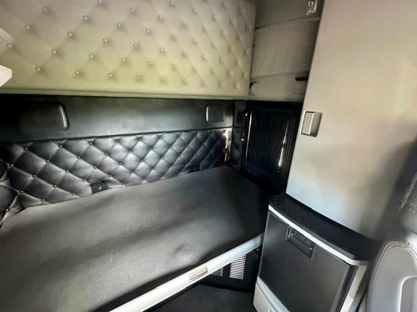 Kenworth T680 sleeper cab interior showing quilted leather paneling, storage cabinet, and bunk area with black upholstery.