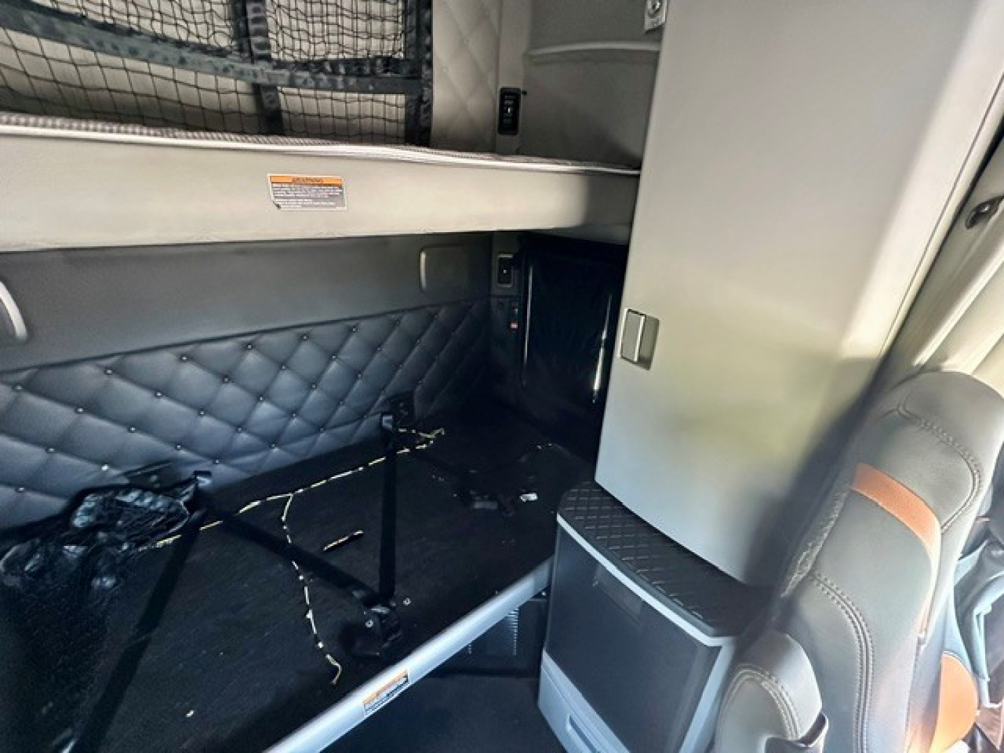 Kenworth T680 sleeper cab interior showing rear storage area with diamond-stitched upholstery and small door, no visible engine or exterior features.
