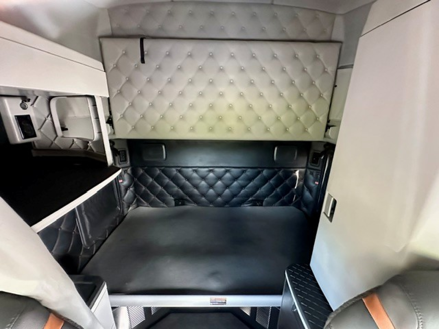 Kenworth T680 truck sleeper cab interior showing a quilted white upper cabinet and a diamond-stitched dark bed area with light gray walls.