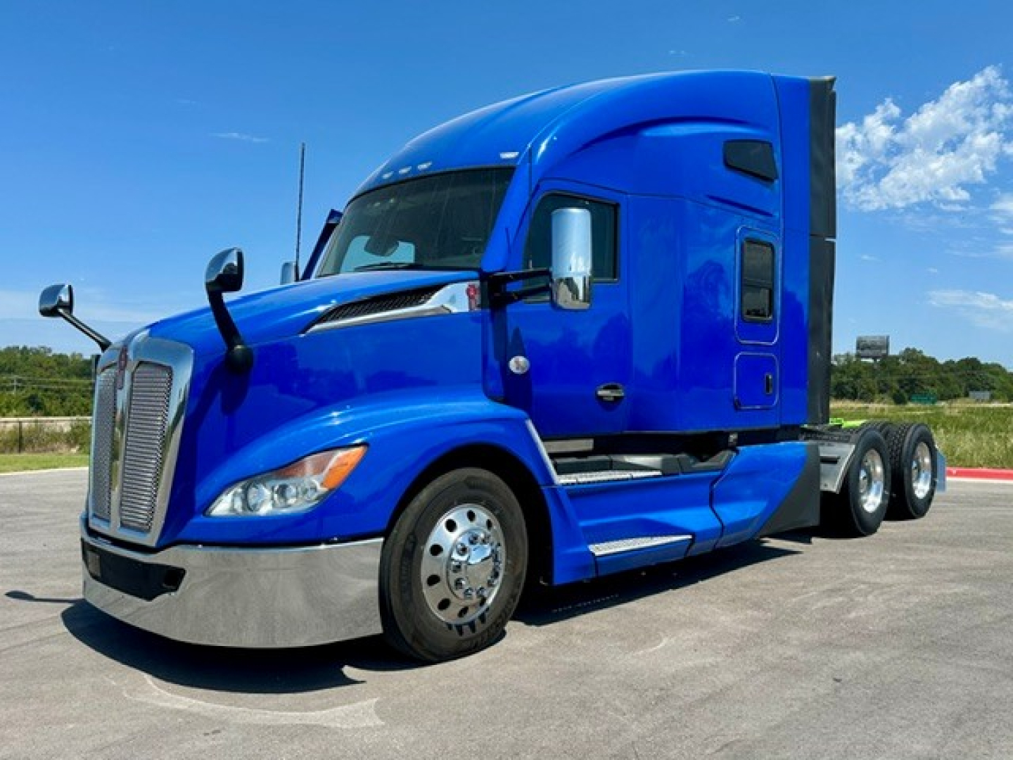 Blue Kenworth T680 tractor cab with sleeper, front left view, chrome bumper, dual rear axles, sleek aerodynamic design, clear sky.