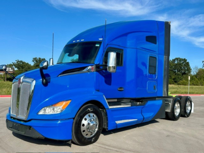 Blue Kenworth T680 tractor cab side view showing grille, windshield, and dual rear axles.