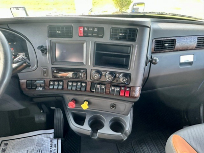 Kennworth T680 truck dashboard view showing infotainment screens, control switches, cup holders, and yellow/red hazard knobs.