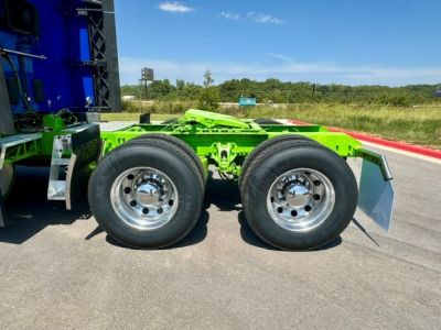 Kenworth truck rear dual wheels with bright green chassis and mud flaps, highway backdrop.