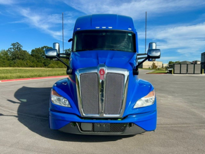Front view of a blue 2023 Kenworth T680 conventional sleeper truck showing chrome grille, headlights, and side mirrors.