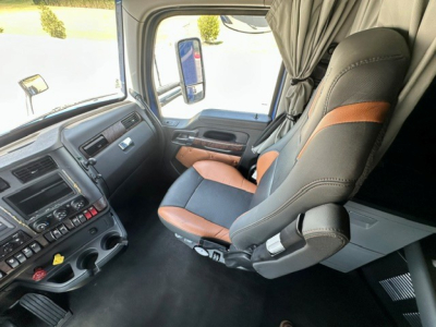 Kenworth T680 cab interior view showing driver seat and dashboard with steering column, various control switches, and side window; front passenger seat and curtain visible.