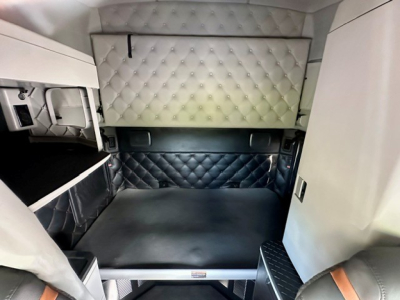Kenworth T680 truck sleeper cab interior showing a quilted white upper cabinet and a diamond-stitched dark bed area with light gray walls.