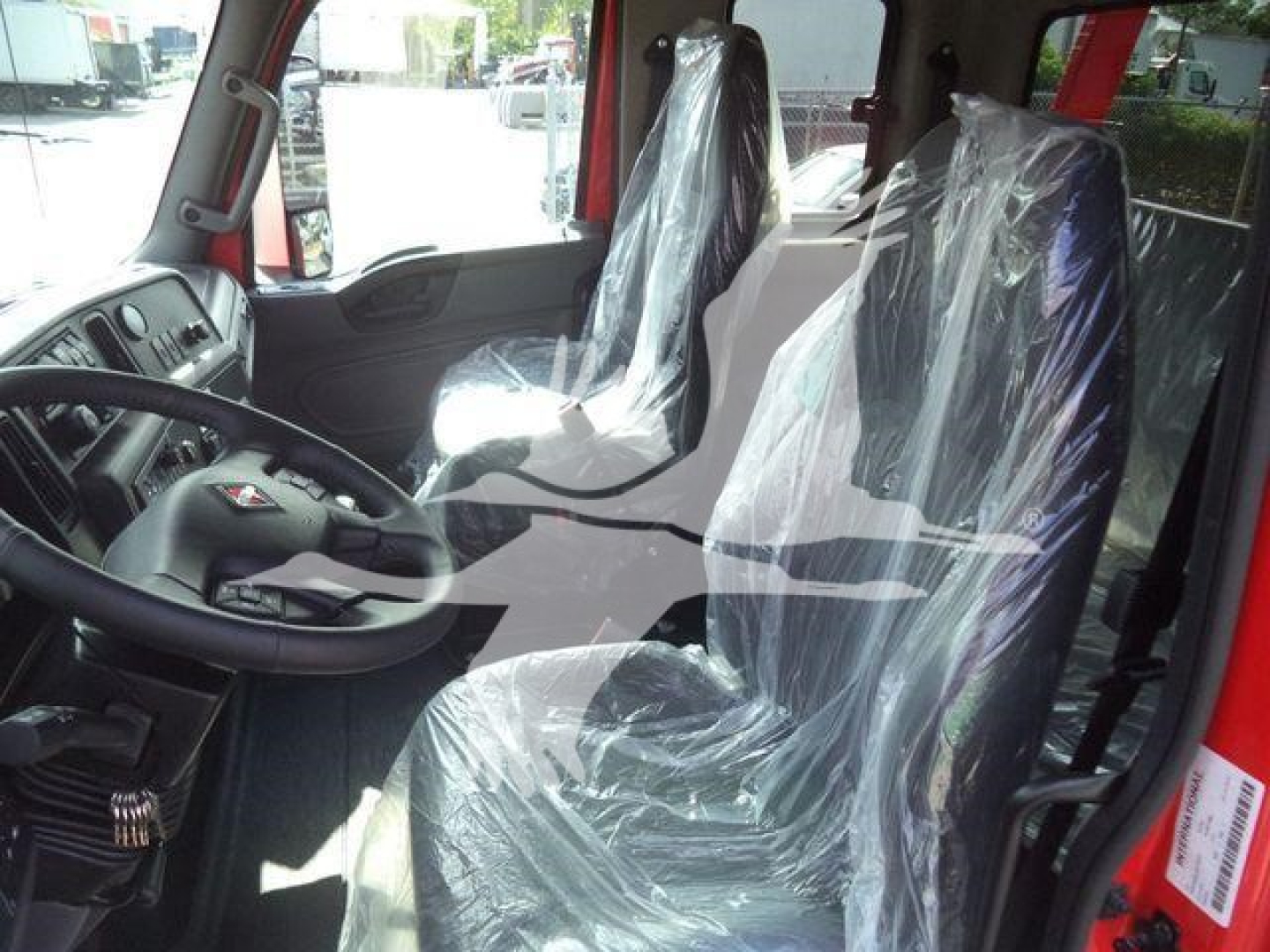 Cab interior of a 2025 International MV truck showing plastic-covered seats and steering wheel.