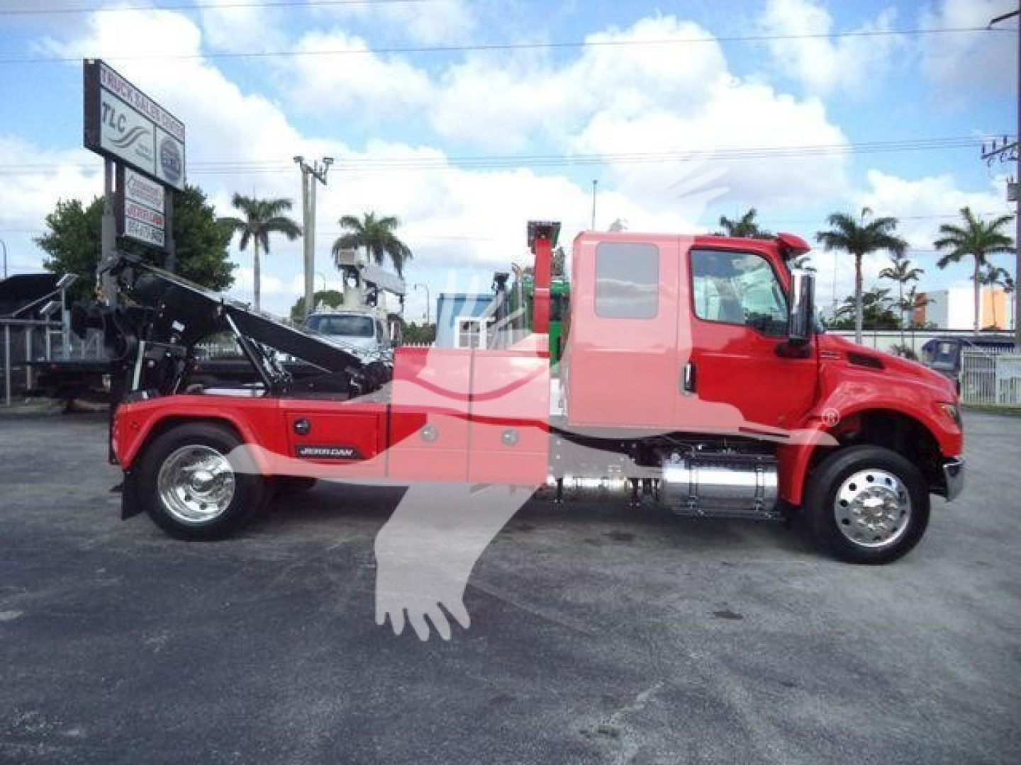 Truck side view showing a red International MV with a winch/rollover wreckers behind cab, stock number MPL60MVEXCABRED, glassy gravel lot.