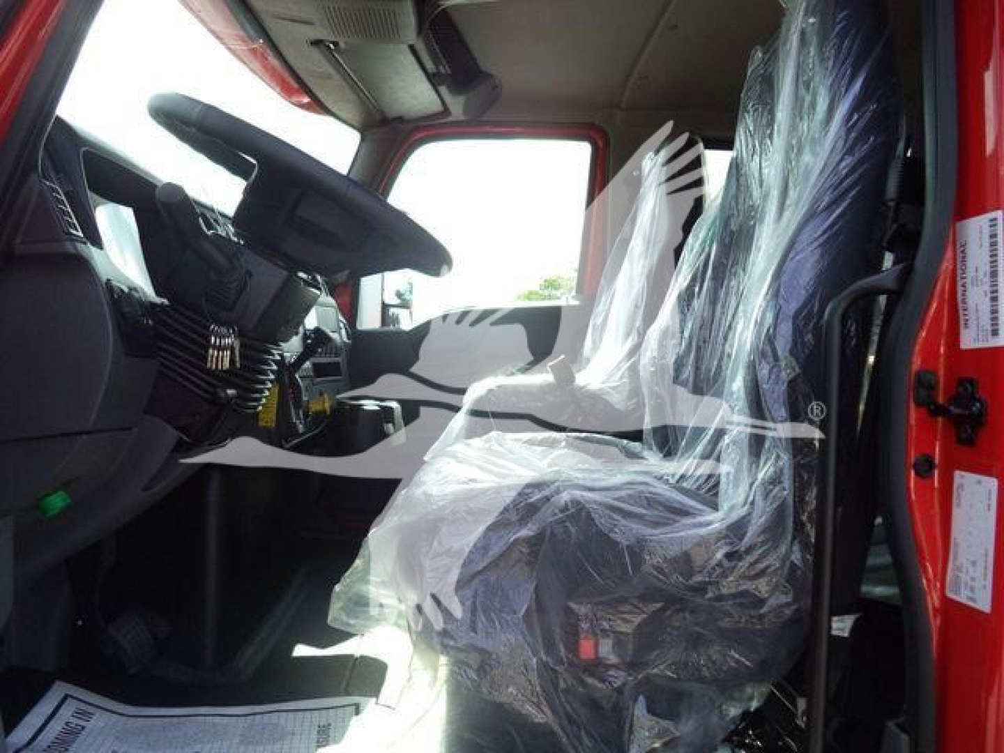Cab interior of a new International MV truck showing plastic-covered seat and steering wheel.