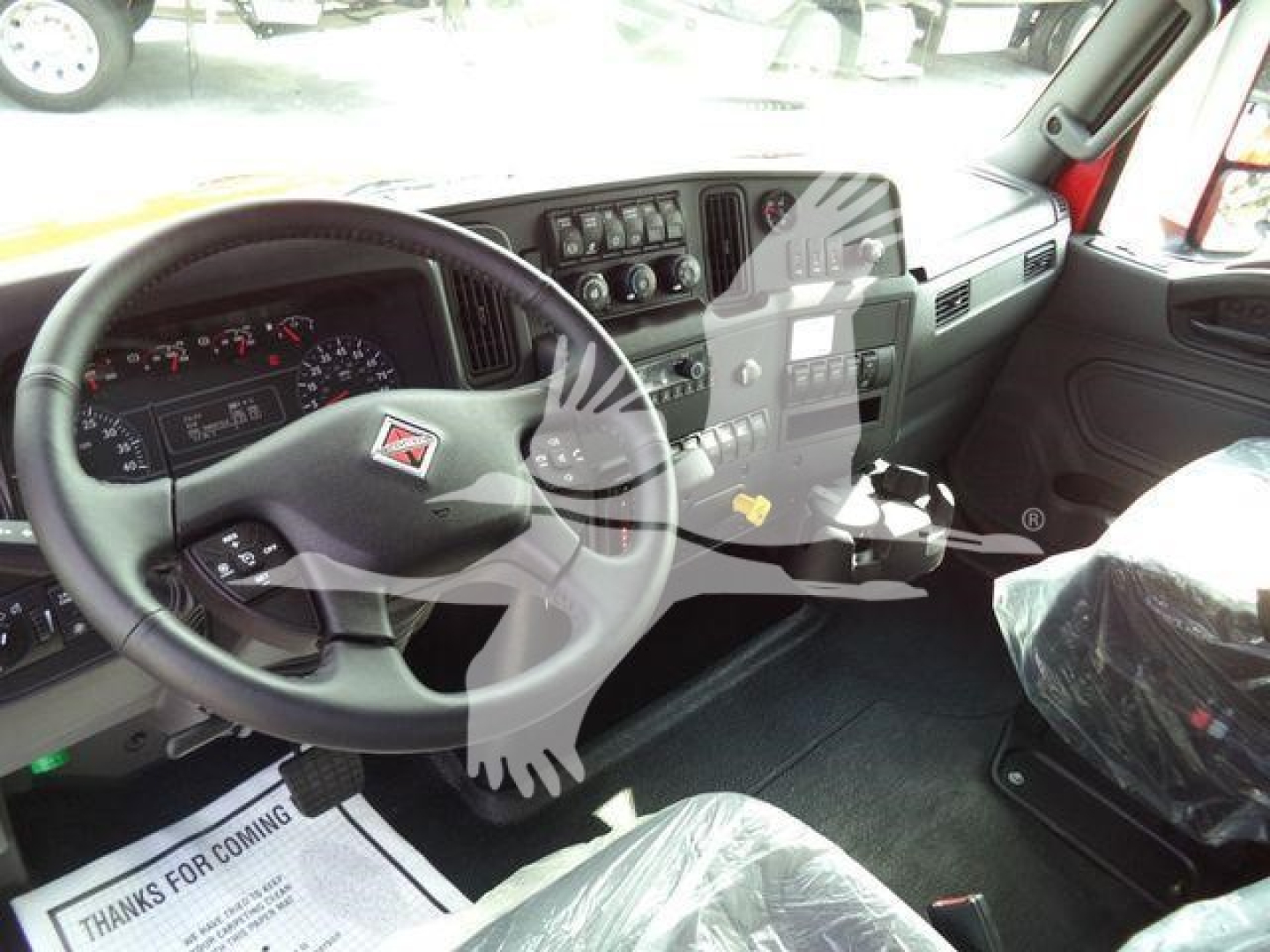 Truck cockpit interior showing steering wheel, dashboard, and center console of a New International MV truck, stock number MPL60MVEXCABRED, winch category.
