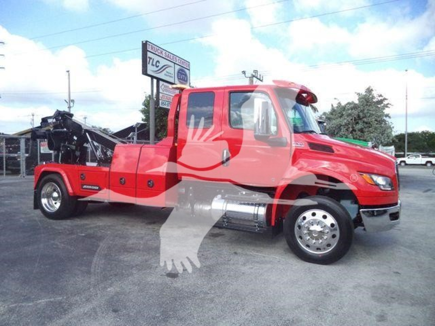 Truck with a red International MV cab and a front-mounted winch, heavy-duty towing boom, large chrome dual tires, daytime exterior.