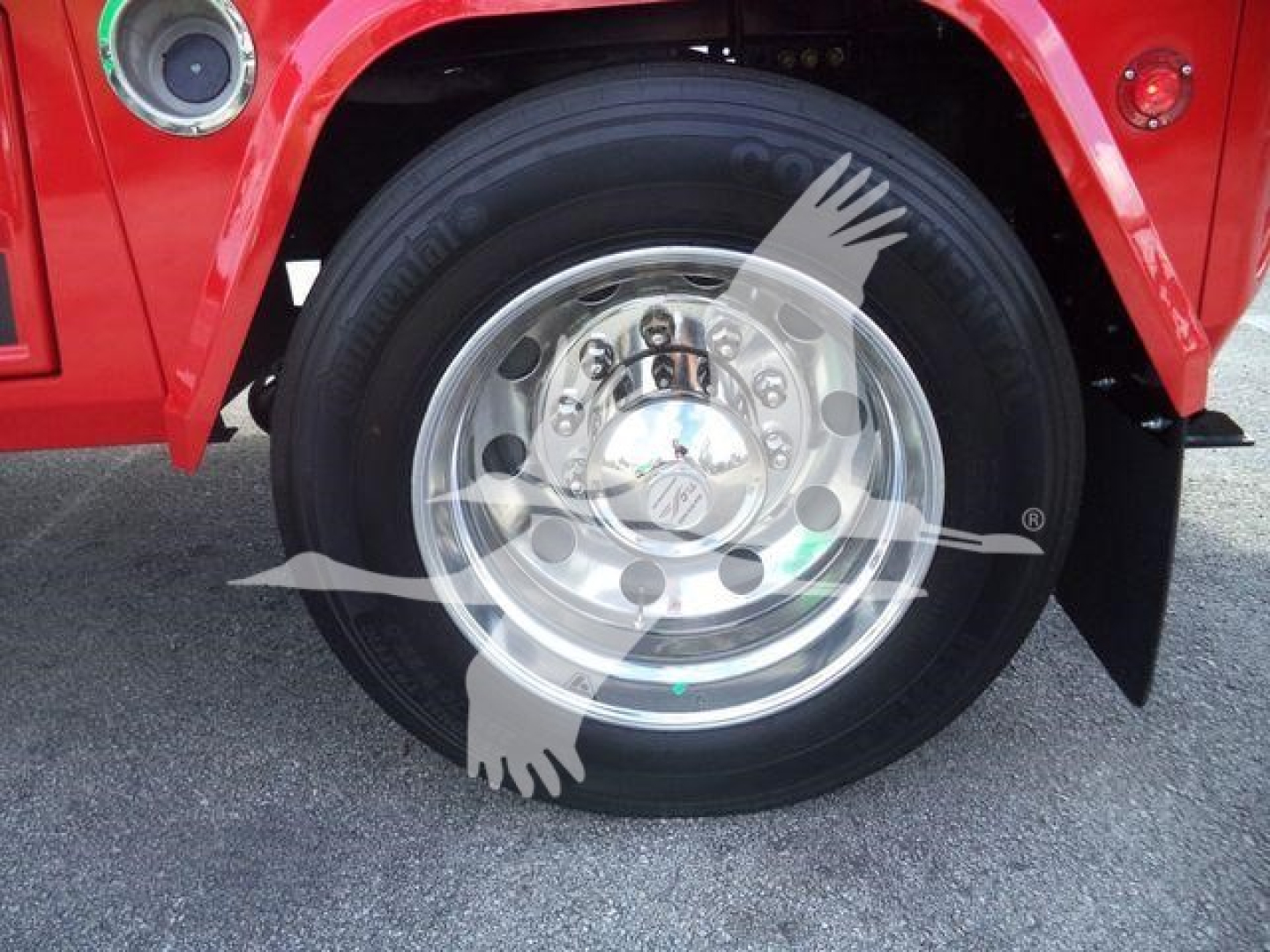 Wheel and front fender of a red International MV truck with chrome hubcap and winch category vehicle.