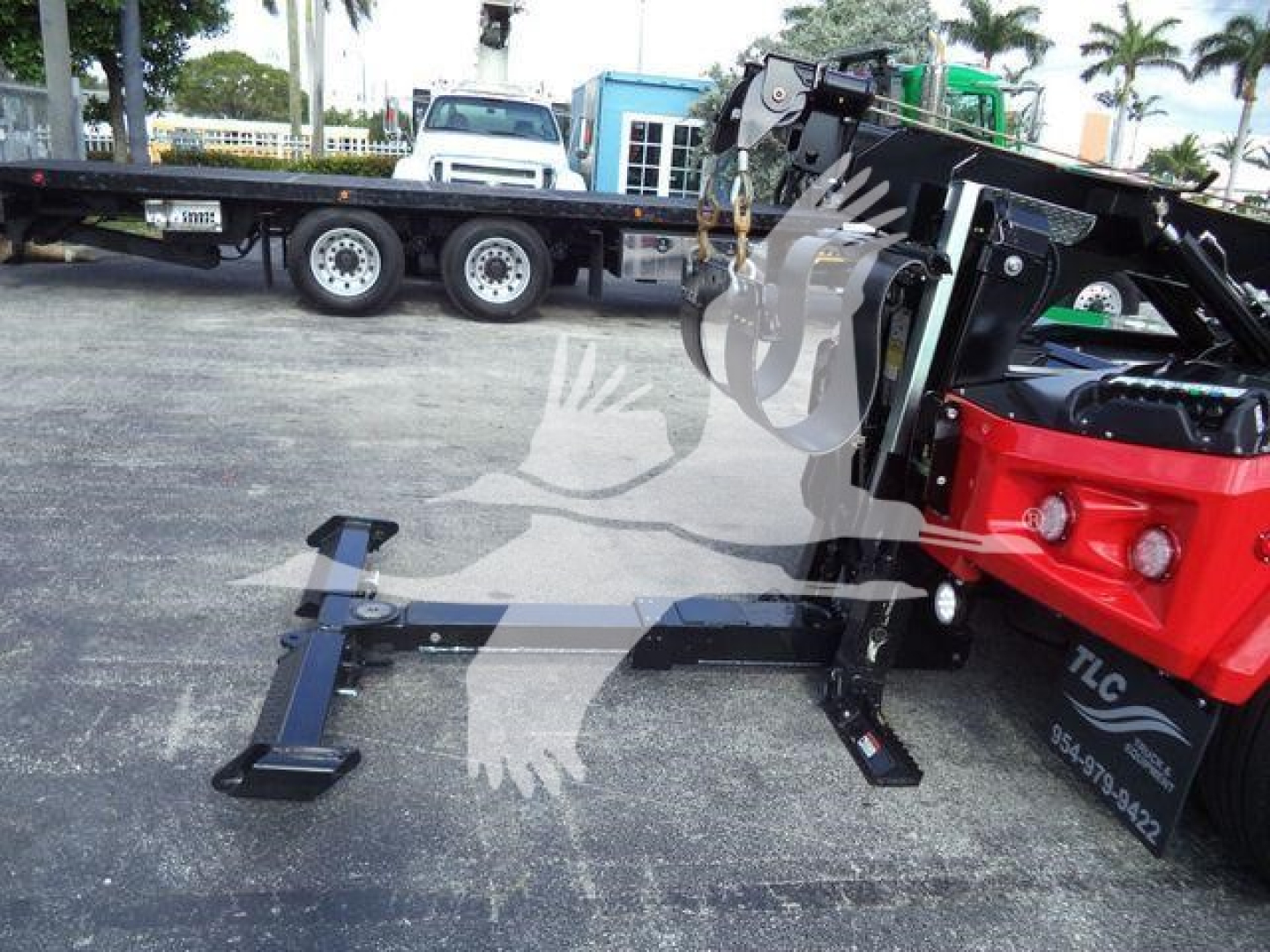 Winch-equipped truck in yard showing front assembly with hydraulic crane and stabilizing legs; visible text includes TLC on black hardware and some numbers on sticker.