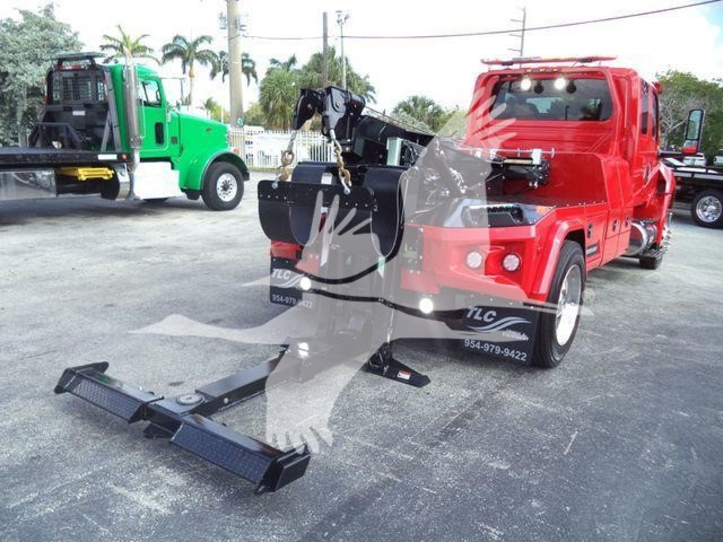 Red International MV tow truck with mounted winch and detached steel tow hooks; black front bumper winch assembly on ground; green truck in background.
