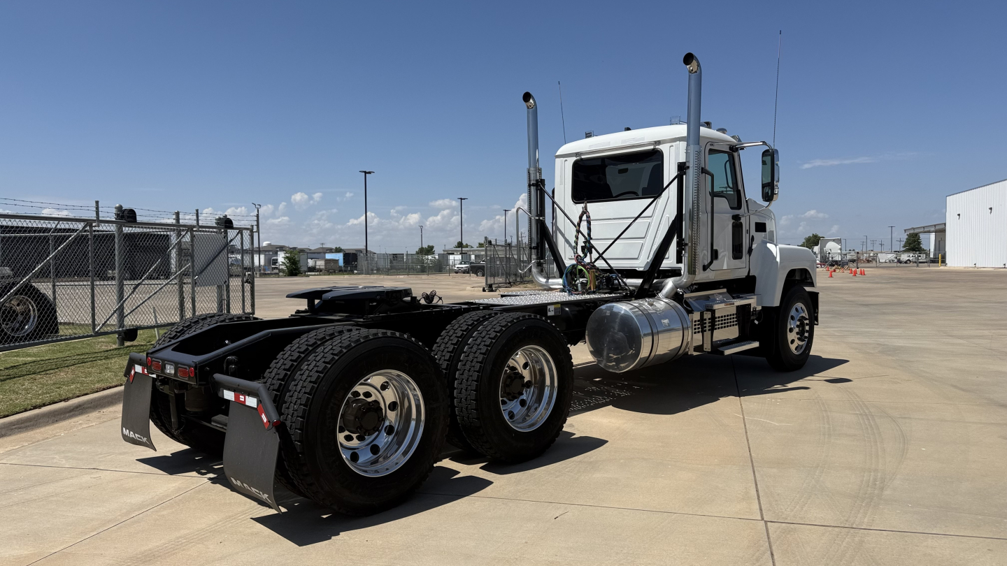 Truck chassis showing rear dual-axle configuration and fuel tanks with fenders; semi-tractor with white cab and vertical exhaust stacks.