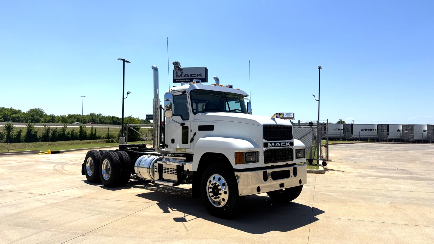Truck chassis and cab in a parking lot showing Mack PI64T badge and front grille.