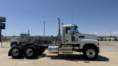 Tractor-trailer chassis side view of a white Mack PI64T day cab truck showing cab, exhaust stack, fuel tanks, and dual rear axles.