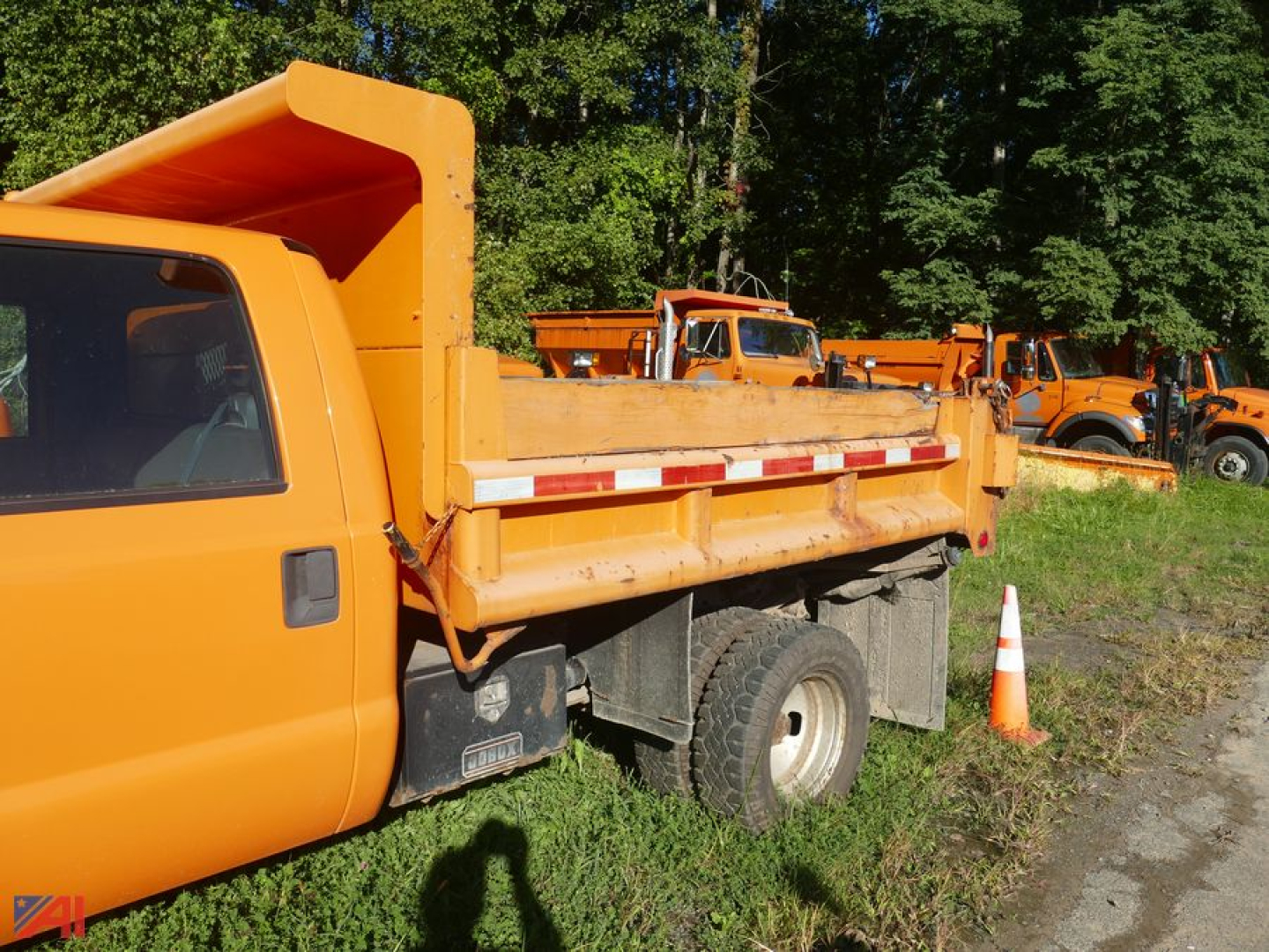 Ford F-350 Super Duty cab and chassis with dual rear wheel and orange dump bed, side view showing rear wheel and orange cones in background.