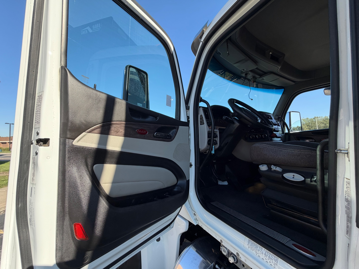 Cabin entry of a Peterbilt 567 truck with open front door, showing steering wheel, dashboard, and seating area.