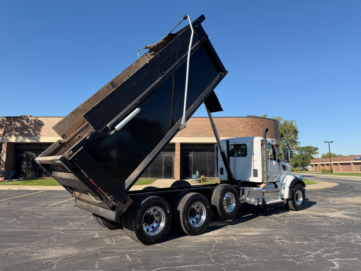 Peterbilt 567 dump truck with bed raised in a parking lot showing three rear axles and chrome wheels