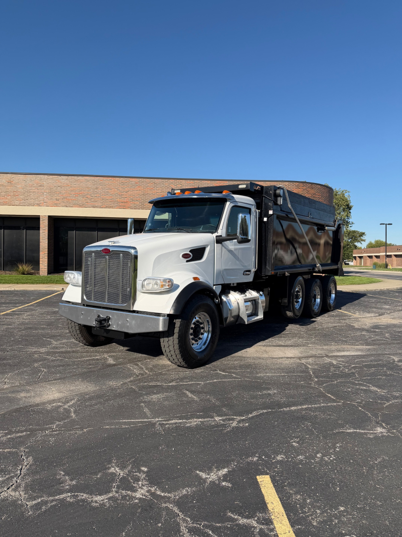 Peterbilt dump truck profile showing a white cab and black dump bed with triple axles and chrome grille; no visible text on the truck body.