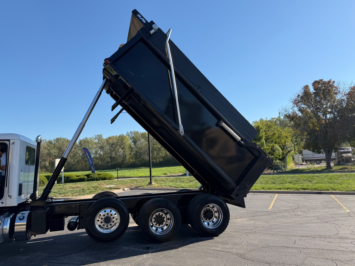 Peterbilt dump truck 3-axle tractor with raised dump bed in a parking lot.