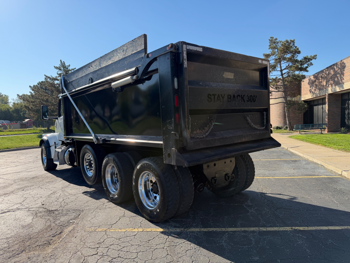 Dump truck rear and side view showing Peterbilt 567 dump bed with black paint and dual rear axles; visible tires and chrome rims; tailgate area with 'STAY BACK' text.