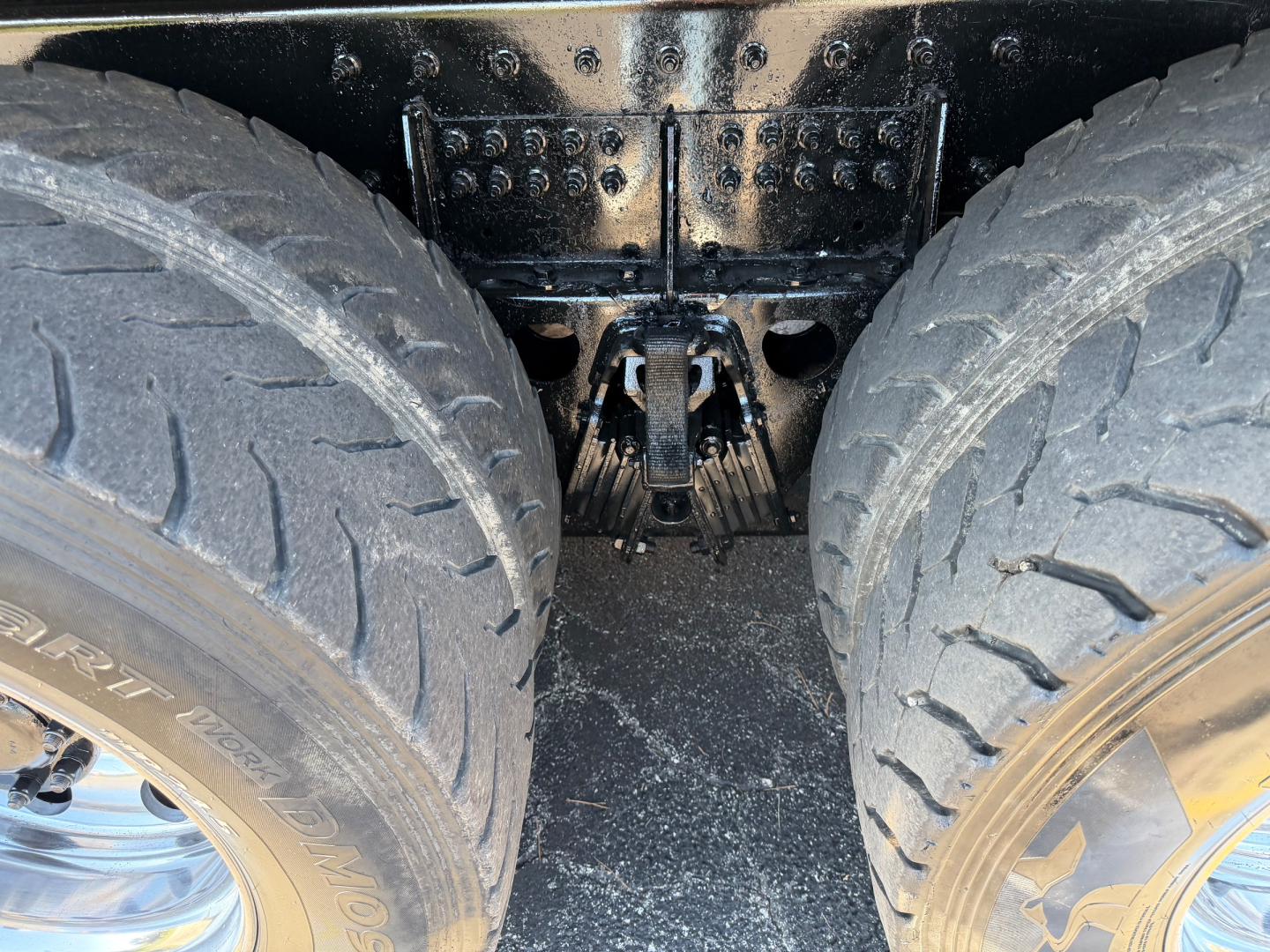 Dual rear wheels and drivetrain area of a Peterbilt truck showing tandem axle with heavy tires and suspension components under a black frame.