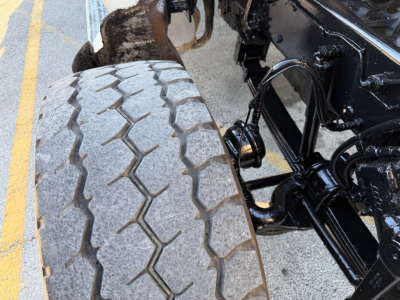 Truck wheel and suspension components of a Peterbilt 567 dump truck showing a rugged tread tire and adjacent chassis framework.