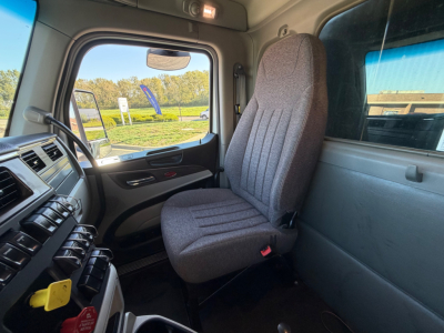 Truck cab interior of a 2023 Peterbilt 567 showing driver's seat and dashboard with steering wheel, window, and controls.