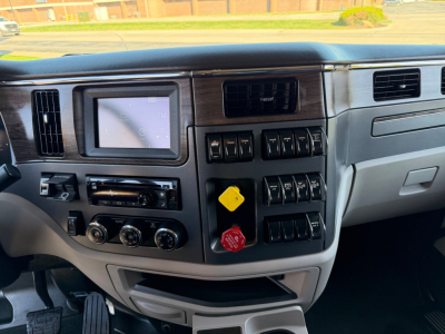 Peterbilt 567 dash/cluster showing gauge cluster display and control switches, buttons, and yellow/red knobs in center console.