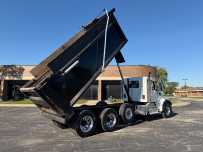 Peterbilt 567 dump truck with bed raised in a parking lot showing three rear axles and chrome wheels