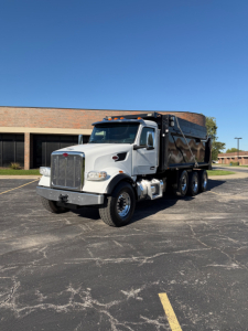 Peterbilt dump truck profile showing a white cab and black dump bed with triple axles and chrome grille; no visible text on the truck body.