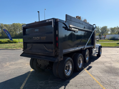 Peterbilt 567 dump truck rear three-quarter view showing dump bed, dual rear axles, and black exterior.