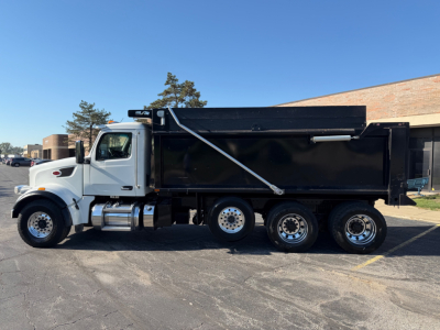 Peterbilt 567 dump truck in side profile with white cab and black dump body. Visible text includes Peterbilt badge on front fender and a chrome fuel tank. No legible serials or model text other than the truck’s shape.