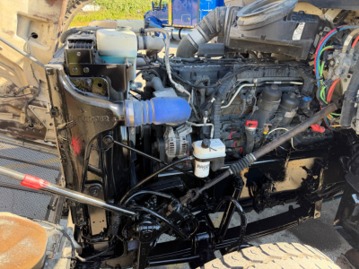 Peterbilt 567 truck engine bay showing coolant reservoir, alternator, hoses, and various engine components.