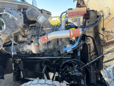 Peterbilt 567 dump truck engine bay showing cooling radiator, hoses, and engine components with Peterbilt badge on the frame.