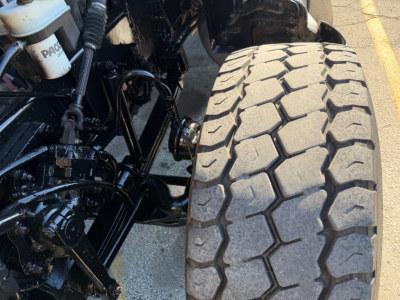 Peterbilt truck wheel and front suspension with tire tread detail visible; hydraulic reservoir and chassis components in view.