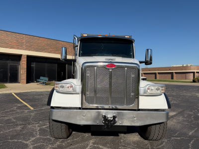 Peterbilt 567 front view showing chrome grille, headlamps, side mirrors, heavy-duty bumper with hitch, and large tires in a parking lot.