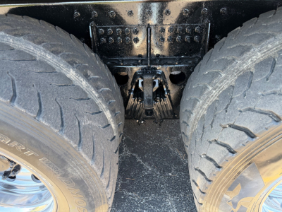 Dual rear wheels and drivetrain area of a Peterbilt truck showing tandem axle with heavy tires and suspension components under a black frame.