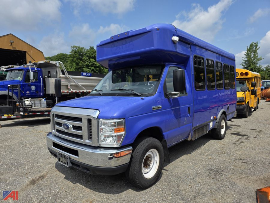 Ford E-Series passenger bus blue exterior, front-left view, with raised roof and large side windows. Ford emblem on grille, headlights, bumper, and wheel wells visible.