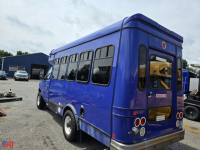 Blue 2018 Ford E-Series passenger bus viewed from rear-left exterior with windows along side and rear door.