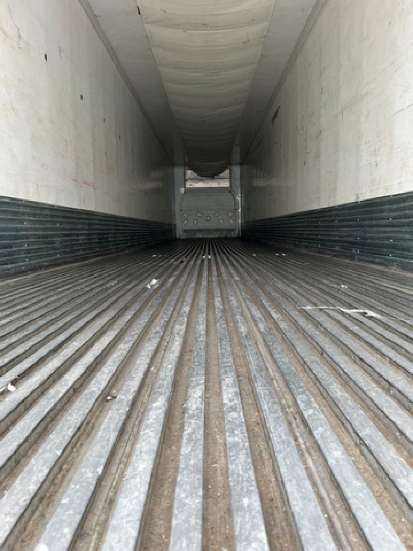 Trailer interior showing ribbed metal floor and white walls with a rear door at the far end; long refrigerated trailer cargo area view.