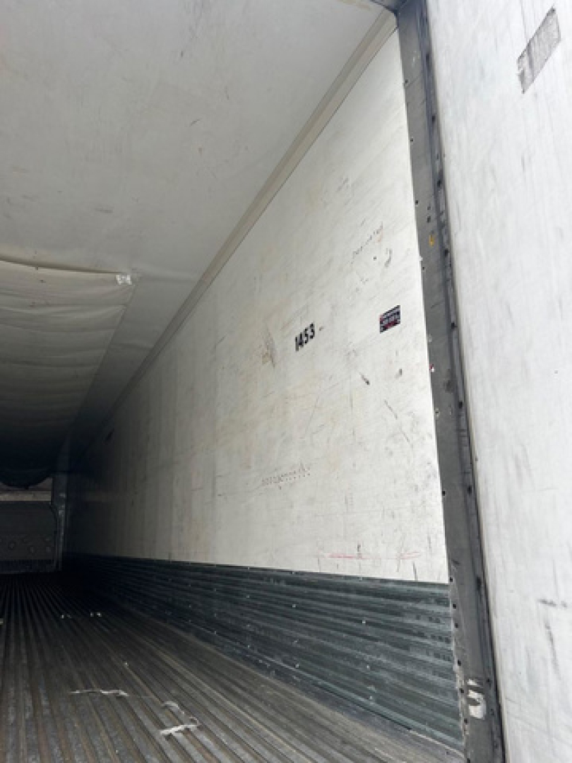 Reefer trailer interior with white insulated walls and ribbed metal floor showing a partial number 1433 and small sticker.