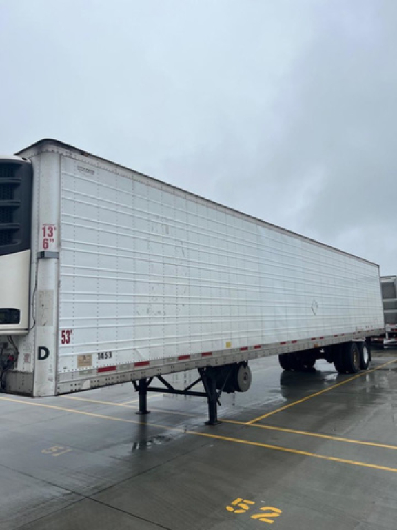 Trailer side view of a 2014 Wabash refrigerated trailer in a lot, with landing gear down and raised wheel axles; white corrugated side panels and refrigeration unit at the front.