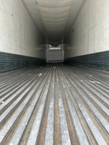 Trailer interior showing ribbed metal floor and white walls with a rear door at the far end; long refrigerated trailer cargo area view.