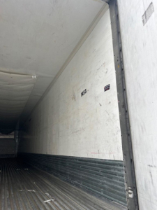 Reefer trailer interior with white insulated walls and ribbed metal floor showing a partial number 1433 and small sticker.