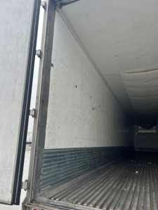Reefer trailer interior showing empty cargo area with ribbed floor and sidewalls; doorway edge visible at left.