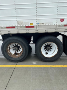 Trailer axle pair of a refrigerated trailer with white wheels and dual tires under a Wabash reefer.